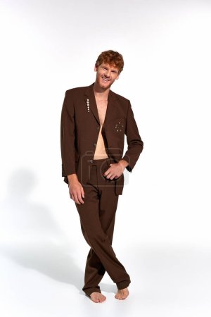 vertikale Aufnahme eines gut aussehenden, fröhlichen Mannes im eleganten Anzug mit Hand am Gürtel, der in die Kamera lächelt, Mode