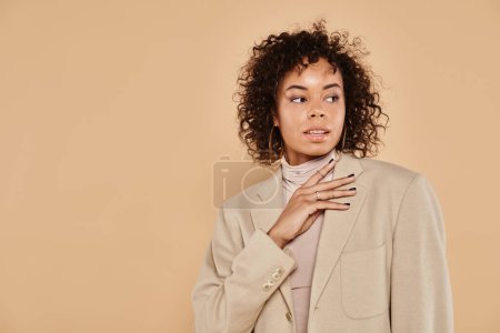 Photo for Brunette african american woman with curly hair posing in turtleneck and blazer on beige background - Royalty Free Image