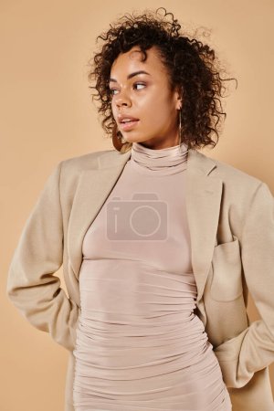 Photo for Stylish african american woman with curly hair posing in autumn dress and blazer on beige backdrop - Royalty Free Image