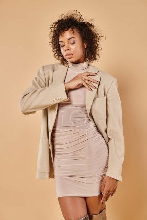 Photo for Autumn fashion, curly african american woman posing in tight dress and blazer on beige backdrop - Royalty Free Image