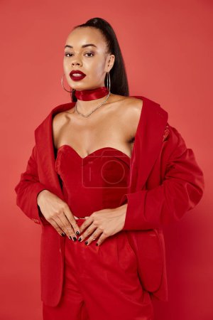 exquisite african american woman with ponytail posing in vibrant suit on red background