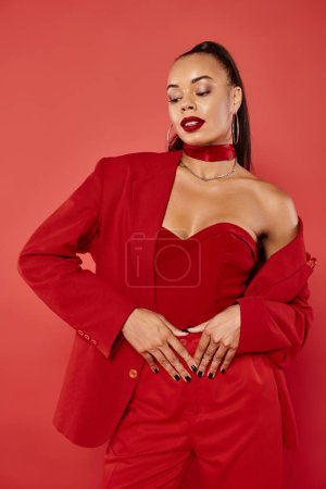 attractive african american woman with ponytail and straight hair posing in suit on red background