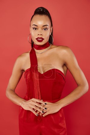 attractive african american woman in vibrant strapless top and pants posing on red background