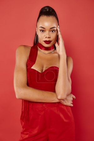 beautiful african american woman in vibrant strapless top and pants posing on red background