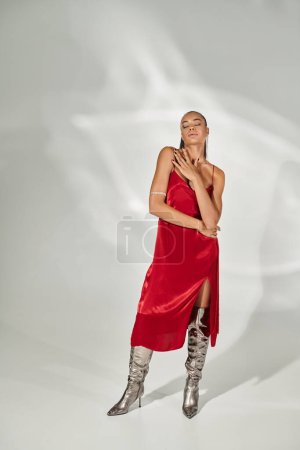 longitud completa de la sensual mujer afroamericana en vestido rojo y botas de plata sobre fondo gris