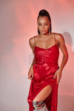 attractive african american woman in red dress looking at camera on grey backdrop with lighting