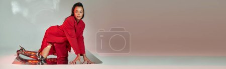 afrikanisch-amerikanisches Model in rotem Blazer, Kleid und silbernen Stiefeln posiert auf verspiegelter Oberfläche, Banner
