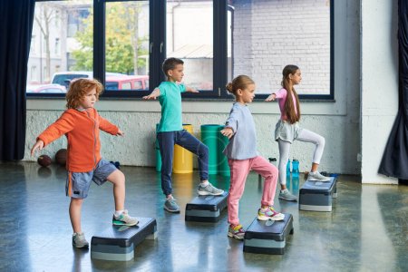 Foto de Cuatro niños bonitos en ropa deportiva ejercicio con pasos de fitness con los brazos a un lado, deporte infantil - Imagen libre de derechos