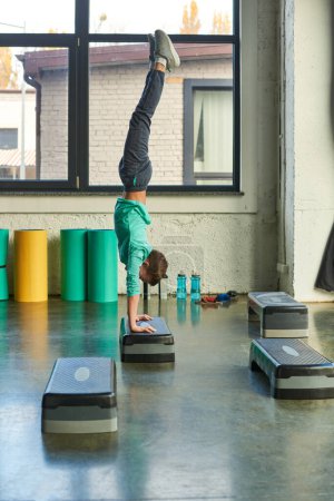 Téléchargez les photos : Plan vertical de petit garçon en tenue de sport debout sur ses mains sur stepper fitness dans la salle de gym, sport - en image libre de droit