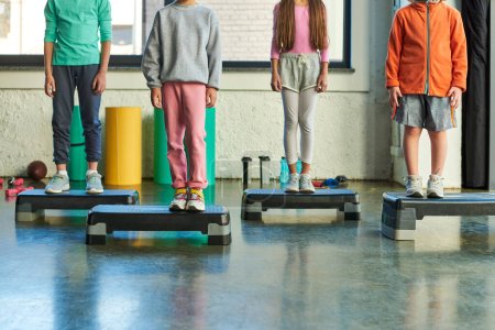 cropped view of four little children in sportswear standing on fitness steppers, child sport