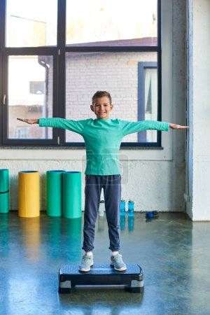 happy little cute boy standing on fitness stepper and smiling joyfully at camera, child sport