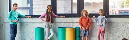 Foto de Niños y niñas lindos preadolescentes en ropa deportiva posando por la ventana en el gimnasio, deporte infantil, pancarta - Imagen libre de derechos