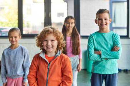quatre enfants préadolescents joyeux posant dans la salle de gym et souriant joyeusement à la caméra, sport pour enfants