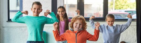 Foto de Cuatro lindos niños pequeños en ropa deportiva jugando músculos y sonriendo a la cámara, deporte infantil, pancarta - Imagen libre de derechos