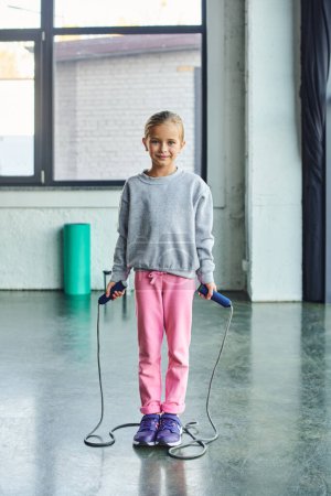 Photo for Pretty preadolescent girl in sportswear with skipping rope in hands, looking at camera, child sport - Royalty Free Image