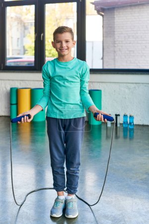 vertical shot of little boy in sportswear with jump rope in hands, smiling at camera, child sport