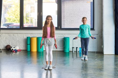 little cute boy and girl in sportswear posing with jump ropes and smiling at camera, child sport