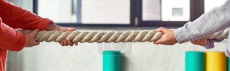 Photo for Cropped view of two children in sportswear pulling fitness rope in gym, child sport, banner - Royalty Free Image