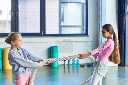 Foto de Dos chicas guapas en ropa deportiva tirando de la cuerda de fitness en el gimnasio y mirándose, deporte infantil - Imagen libre de derechos