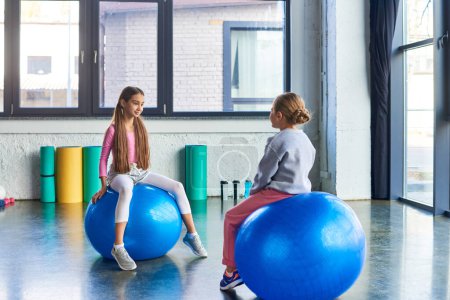 pretty little girls in sportswear sitting on fitness balls and looking at each other, child sport puzzle 677583474