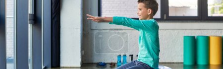 Photo for Cute preadolescent boy in blue sportswear posing in profile and exercising, child sport, banner - Royalty Free Image