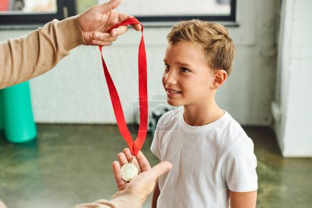 abgeschnittene Ansicht eines Mannes, der eine goldene Medaille an vorpubertierende süße Jungen in Sportbekleidung, Kindersport vergibt