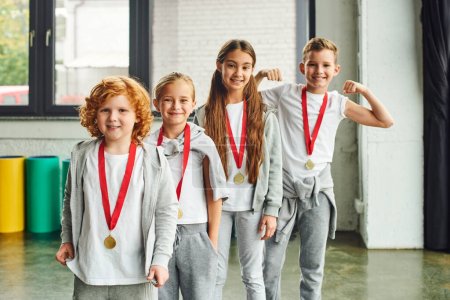 fröhliche Kinder in Sportbekleidung mit goldenen Medaillen, die fröhlich in die Kamera lächeln, Kindersport