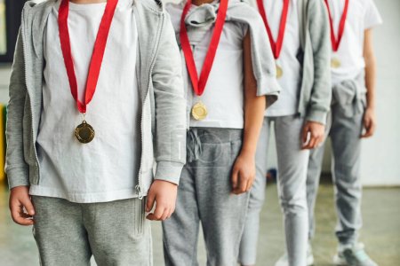 vista recortada de cuatro niños en ropa deportiva con medallas de oro en el cuello, deporte infantil