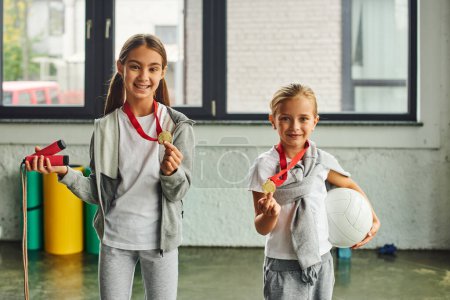 cute preadolescent girls posing with golden medals with jump rope and volleyball in hands, sport