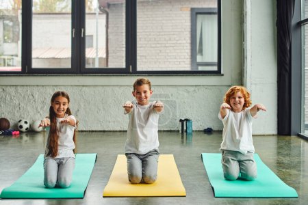 Photo for Little joyful children sitting on fitness mats and stretching arms, smiling at camera, child sport - Royalty Free Image