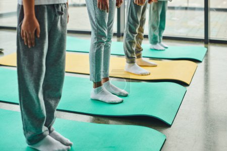 recortado cuatro niños preadolescentes en ropa deportiva de pie sobre alfombras de fitness, deporte infantil