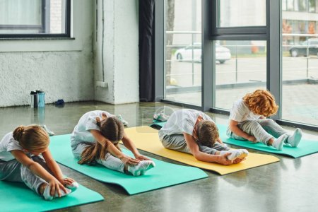 preadolescent cute boys and girls sitting on fitness mats and stretching actively, child sport