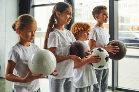 four cute preadolescent children with different kinds of balls posing in profile, child sport