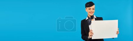 Photo for Elegant stewardess in professional outfit standing with empty poster on blue backdrop, banner - Royalty Free Image