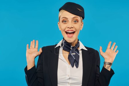 Photo for Portrait of amazed and joyful stewardess in uniform showing wow gesture on blue background - Royalty Free Image