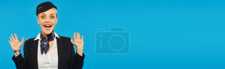 Photo for Portrait of astonished stewardess in uniform showing wow gesture on blue backdrop, banner - Royalty Free Image