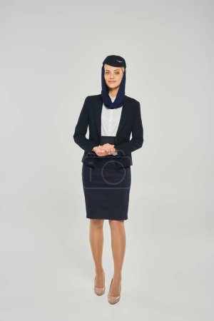 full length of young woman in elegant uniform of arabian airlines stewardess on grey backdrop