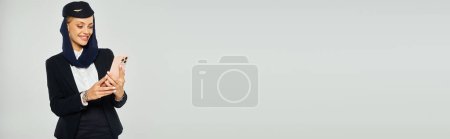 Téléchargez les photos : Hôtesse de l'air heureuse en uniforme des compagnies arabes bavardant sur téléphone portable sur fond gris, bannière - en image libre de droit