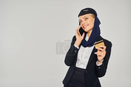 happy arabian airlines stewardess in uniform with credit card talking on smartphone on grey