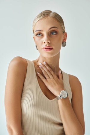 stylish woman with perfect skin and natural makeup posing with hand on chest looking away on grey