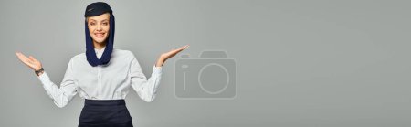 Téléchargez les photos : Accueillante hôtesse de l'air arabe en foulard et uniforme posant à bras ouverts sur gris, bannière - en image libre de droit
