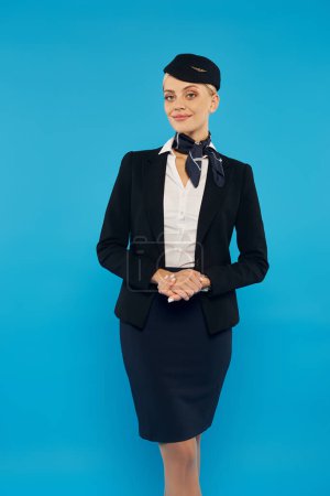 female flight attendant in elegant uniform smiling at camera while standing on grey backdrop
