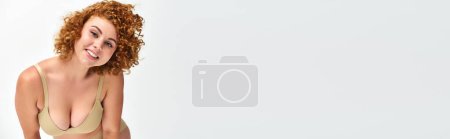 Téléchargez les photos : Excité rousse femme avec corps incurvé et buste regardant caméra sur blanc, bannière horizontale - en image libre de droit