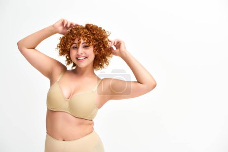 Photo for Carefree redhead woman with beautiful curvy body posing in beige lingerie on white, self-confidence - Royalty Free Image
