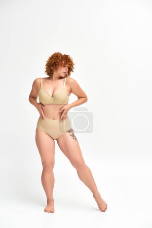 Téléchargez les photos : Pleine longueur de femme rousse séduisante avec un corps tatoué incurvé sur blanc, beauté non traditionnelle - en image libre de droit