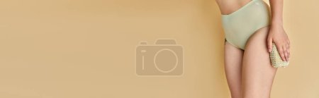 Téléchargez les photos : Vue partielle de femme courbée en culotte taupe tenant un gant de toilette sur fond beige, bannière horizontale - en image libre de droit