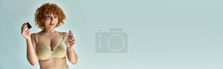 séduisante femme rousse en soutien-gorge beige avec un corps incurvé pulvérisation parfum sur gris, bannière horizontale
