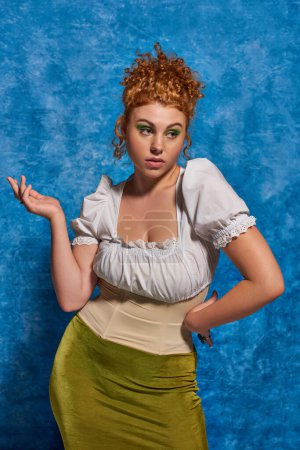confused plus size model with red wavy hair standing with hands on hip on blue textured backdrop
