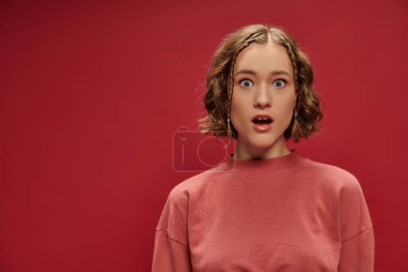 portrait of young and shocked woman with short wavy hair and braids on red background, surprise