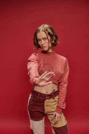 Photo for Personal style, pretty girl in patchwork pants and cropped long sleeve showing no gesture on red - Royalty Free Image